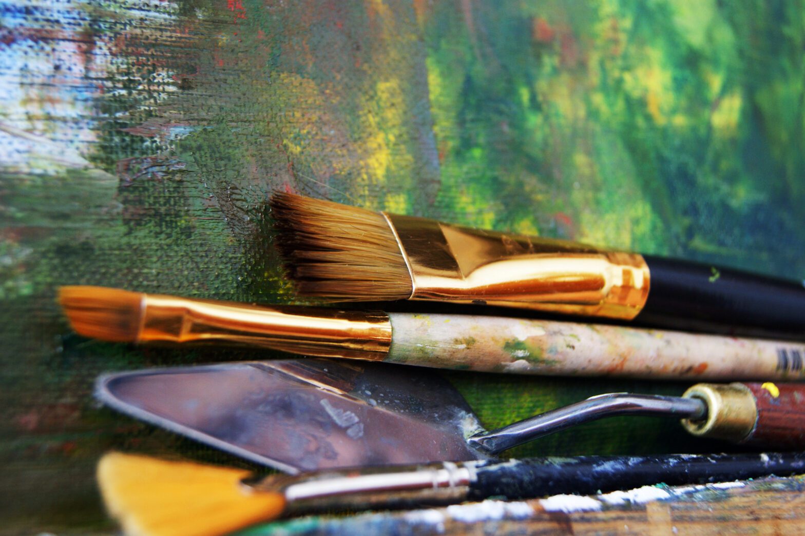 An image of paintbrushes and other painting tools sitting on top of a painted canvas.
