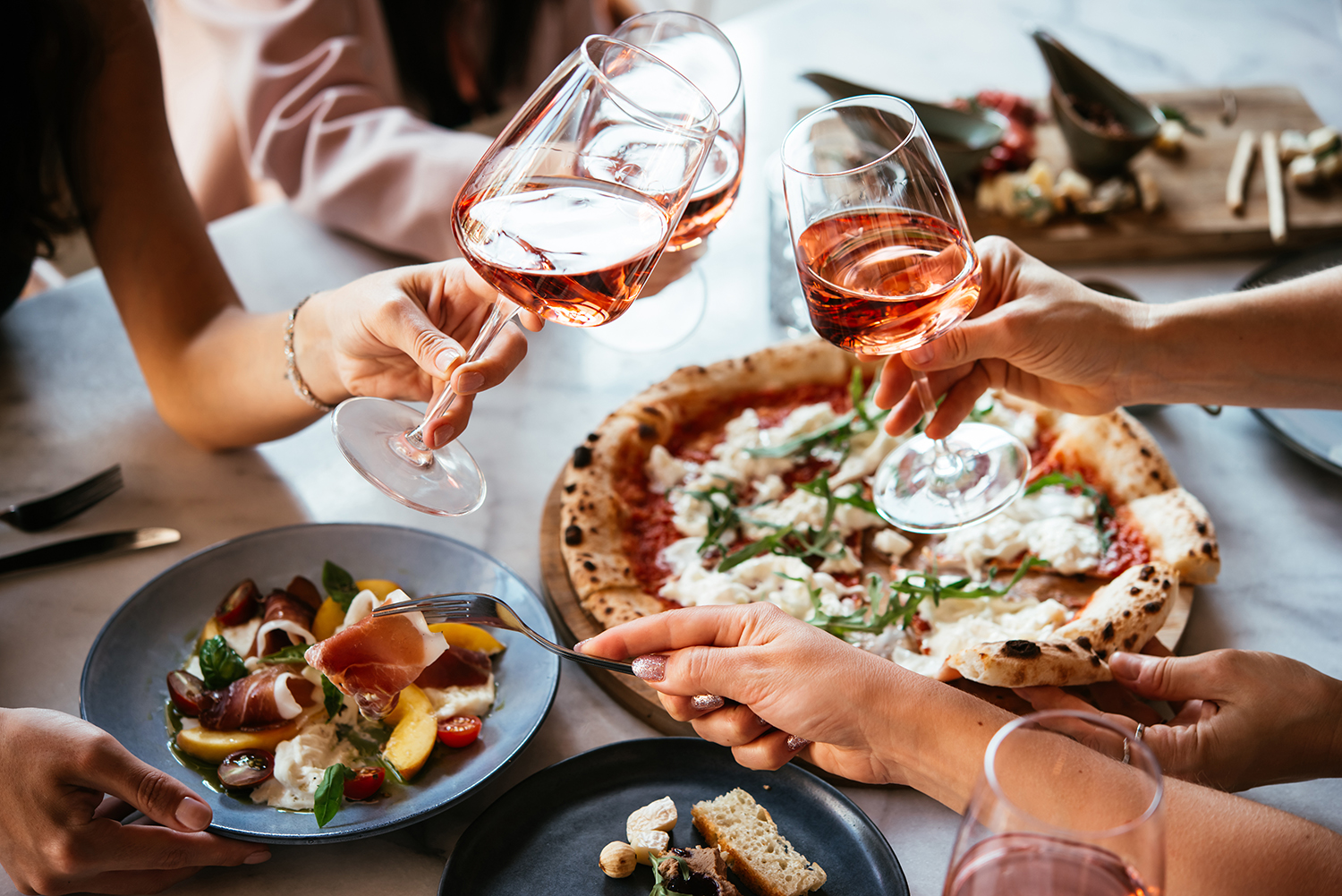 People sharing a glass of wine over an excellent spread of food, including a gourmet pizza, on a table.